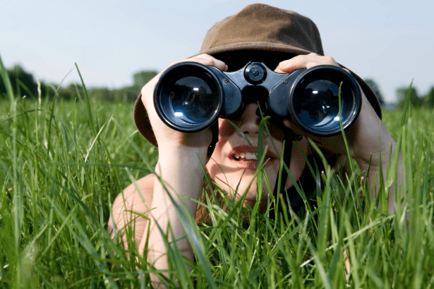 lady laying in deep grass with looking through binoculars